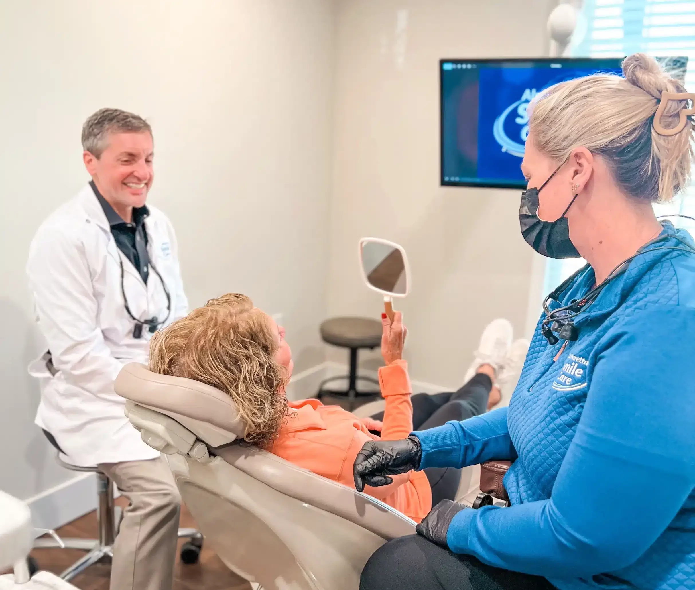 Dentist and hygienist showing a patient her smile in a hand mirror