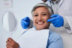 Smiling senior woman holding a mirror at the dentist