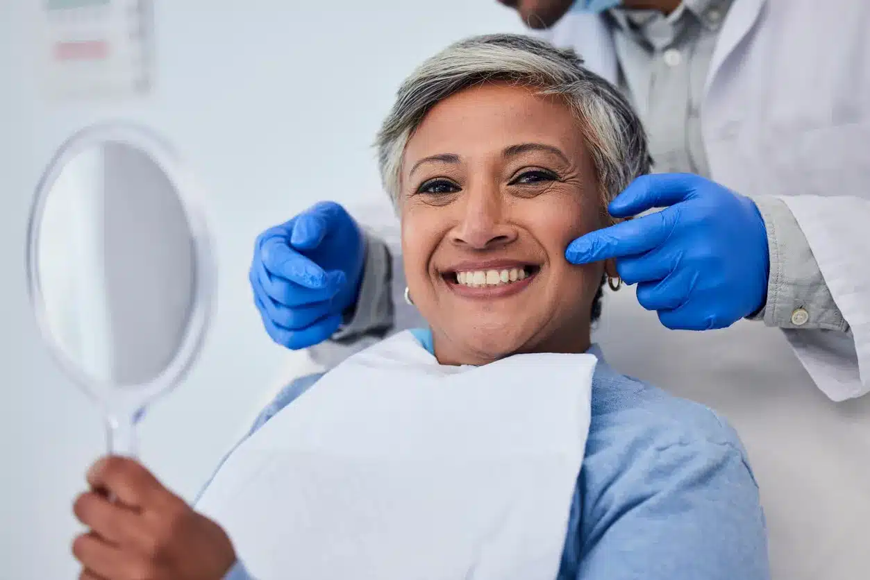 Smiling senior woman holding a mirror at the dentist