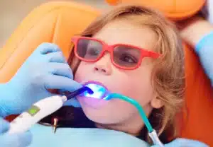 Child in protective glasses receiving dental sealants